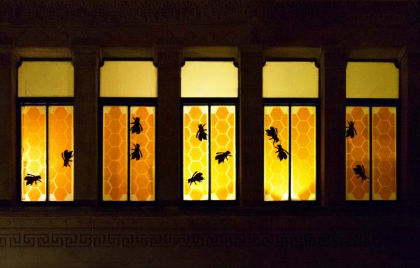 Five narrow vertical windows lit from the inside, decorated with yellow/orange honeycomb backgrounds and black silhouetted bees
