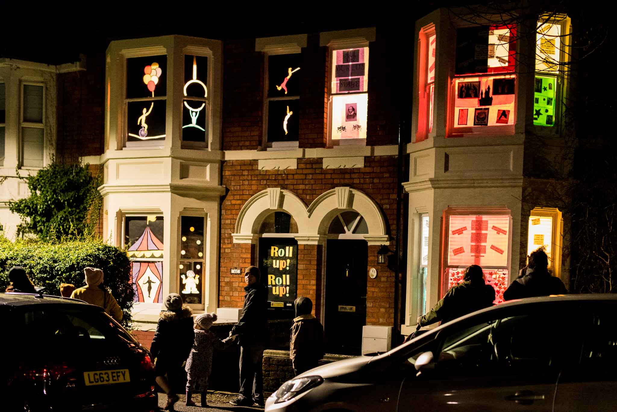 People wandering past house displaying colourful scenes lit up at night time